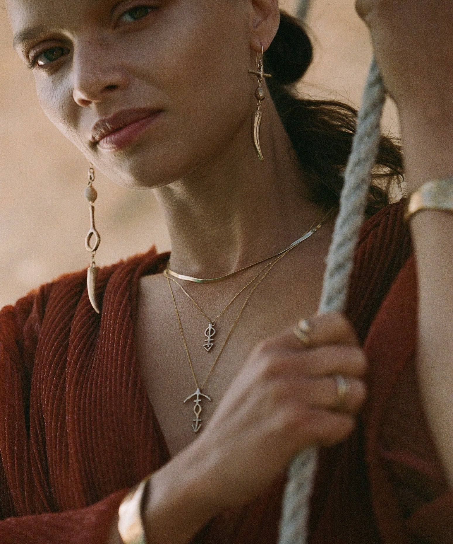 Close up of a model wearing layered gold talisman necklaces, long horn drop earrings and a gold cuff by Catori Life.
