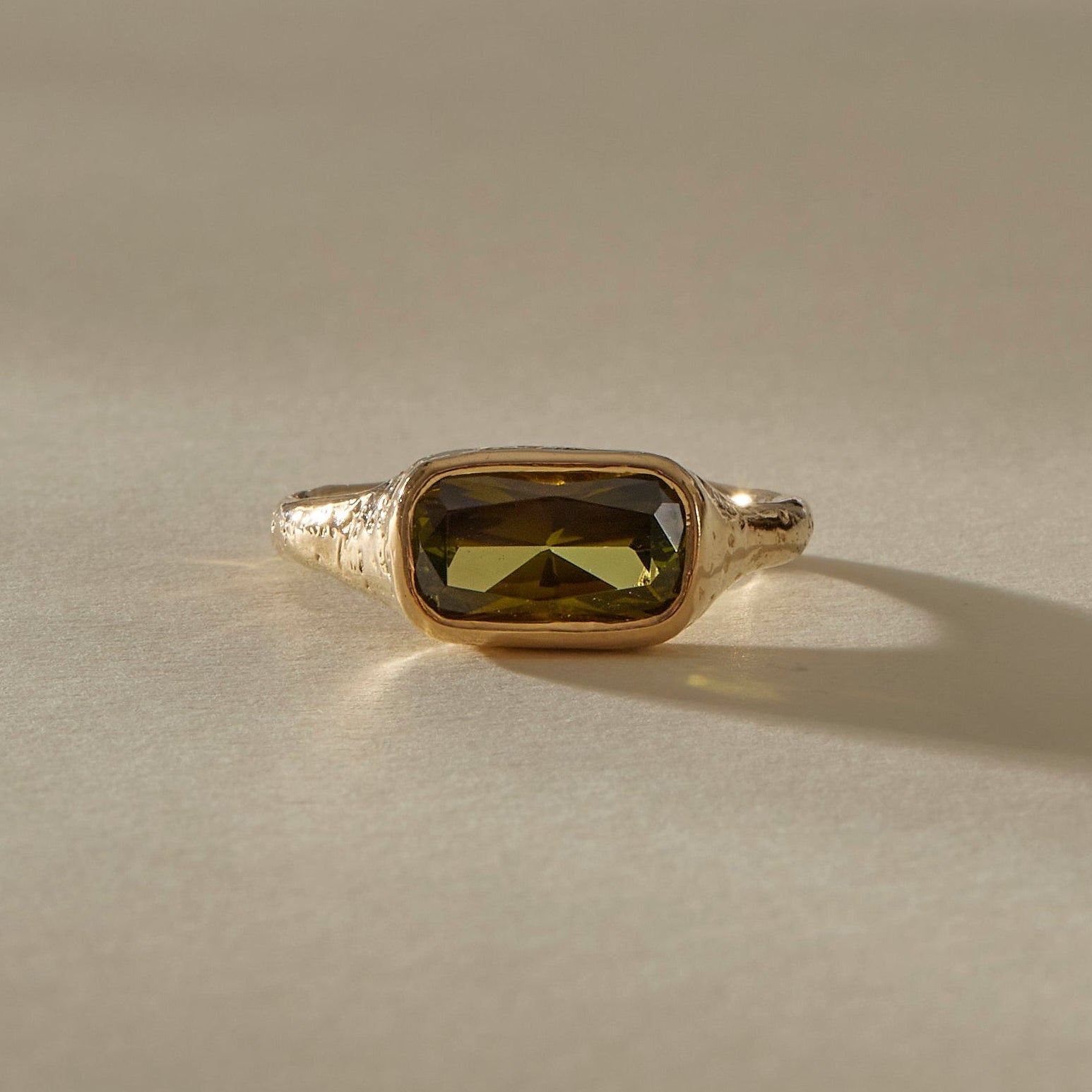 Gold ring with a green gemstone on a beige background