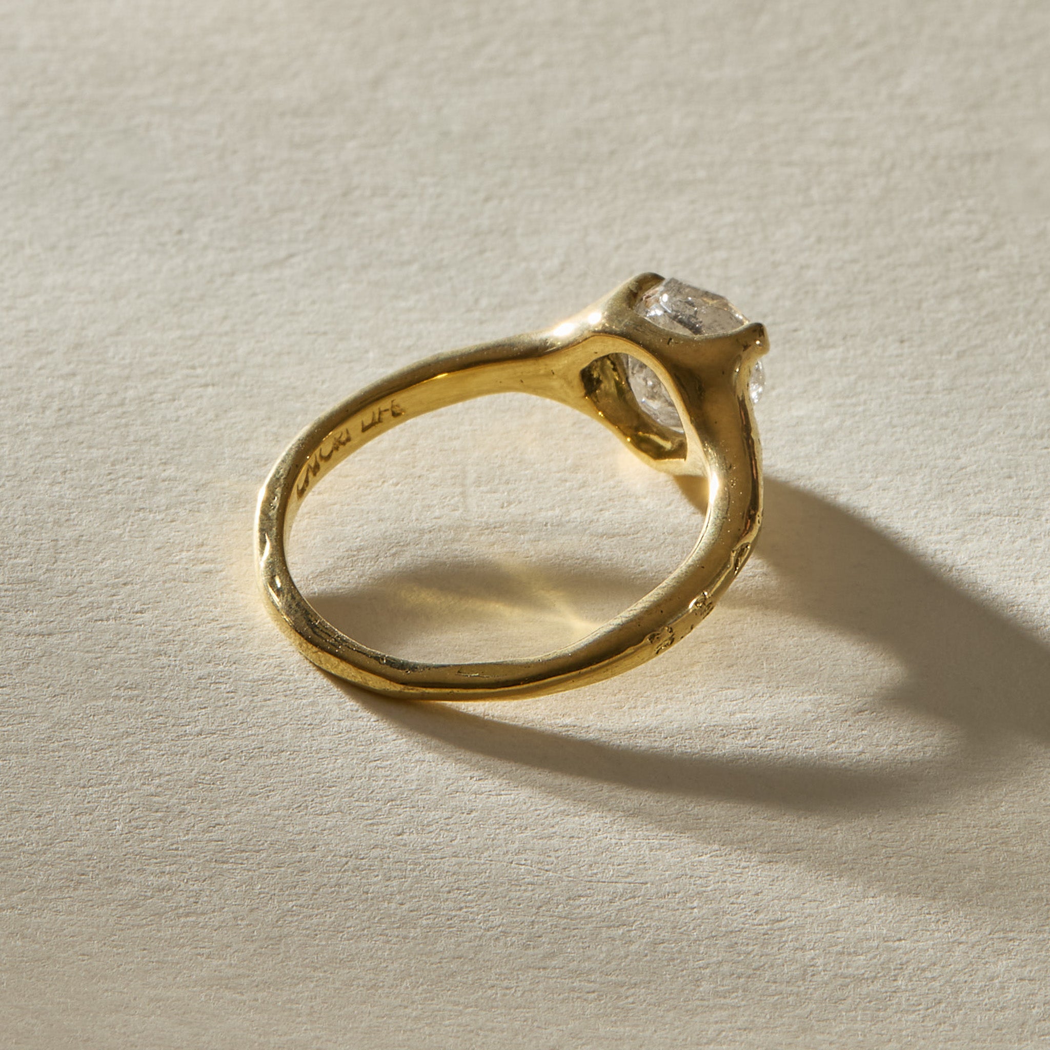 Amara Ring in 18k recycled gold from behind, with the molten band curving up around the diamond setting.