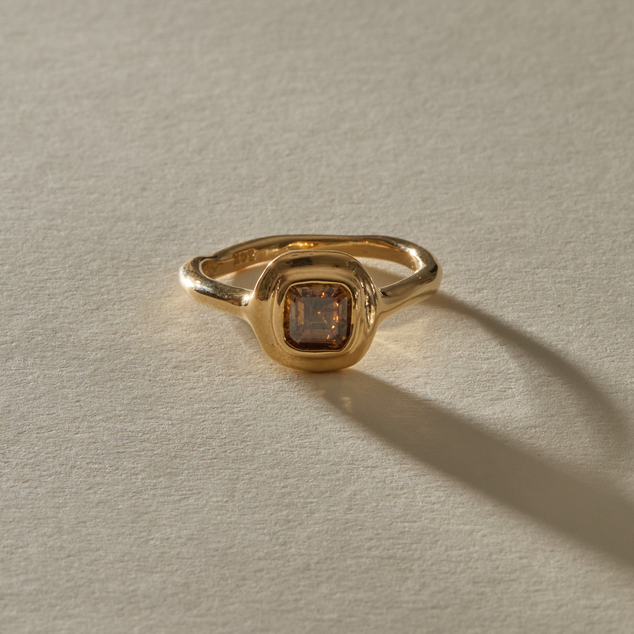 Ambre champagne diamond ring from the front, showing the square step cut stone in its rounded gold bezel.