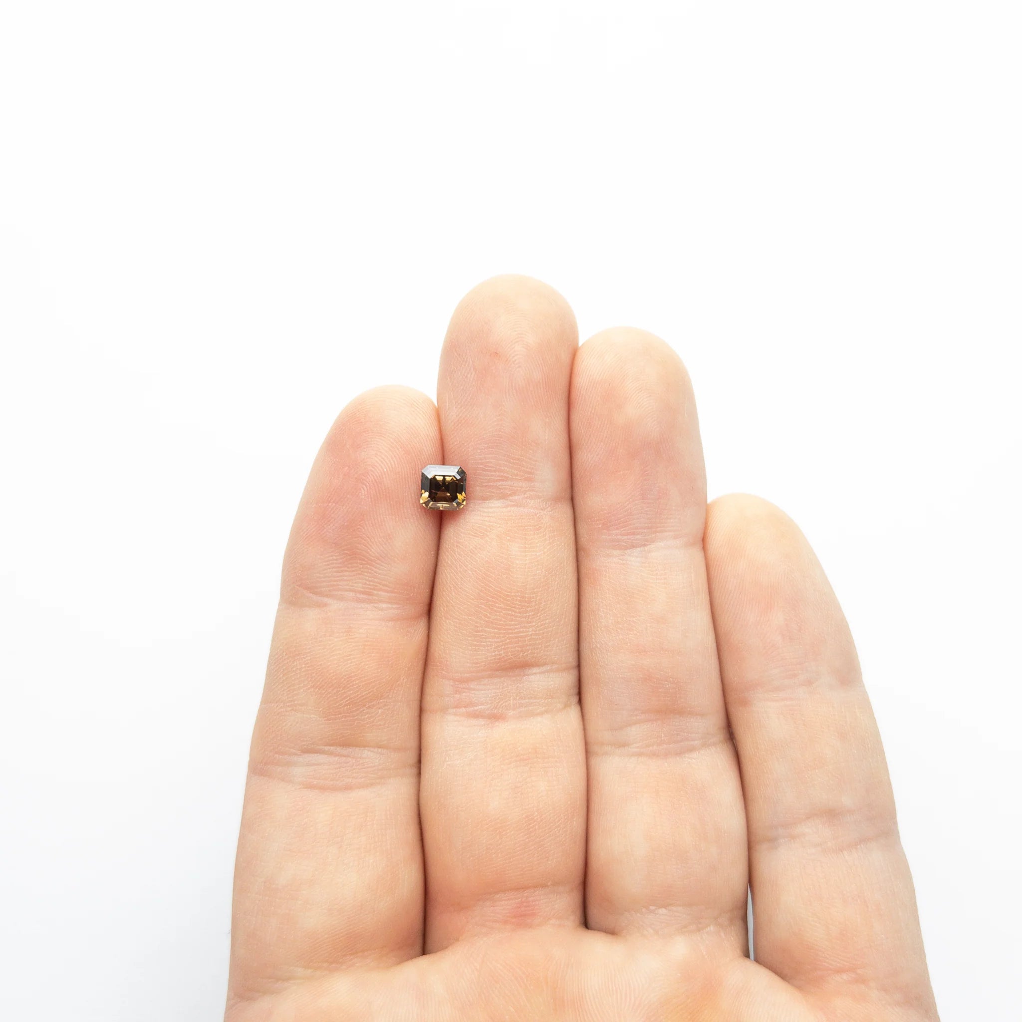 The loose champagne step cut diamond resting on fingertips to show its size.