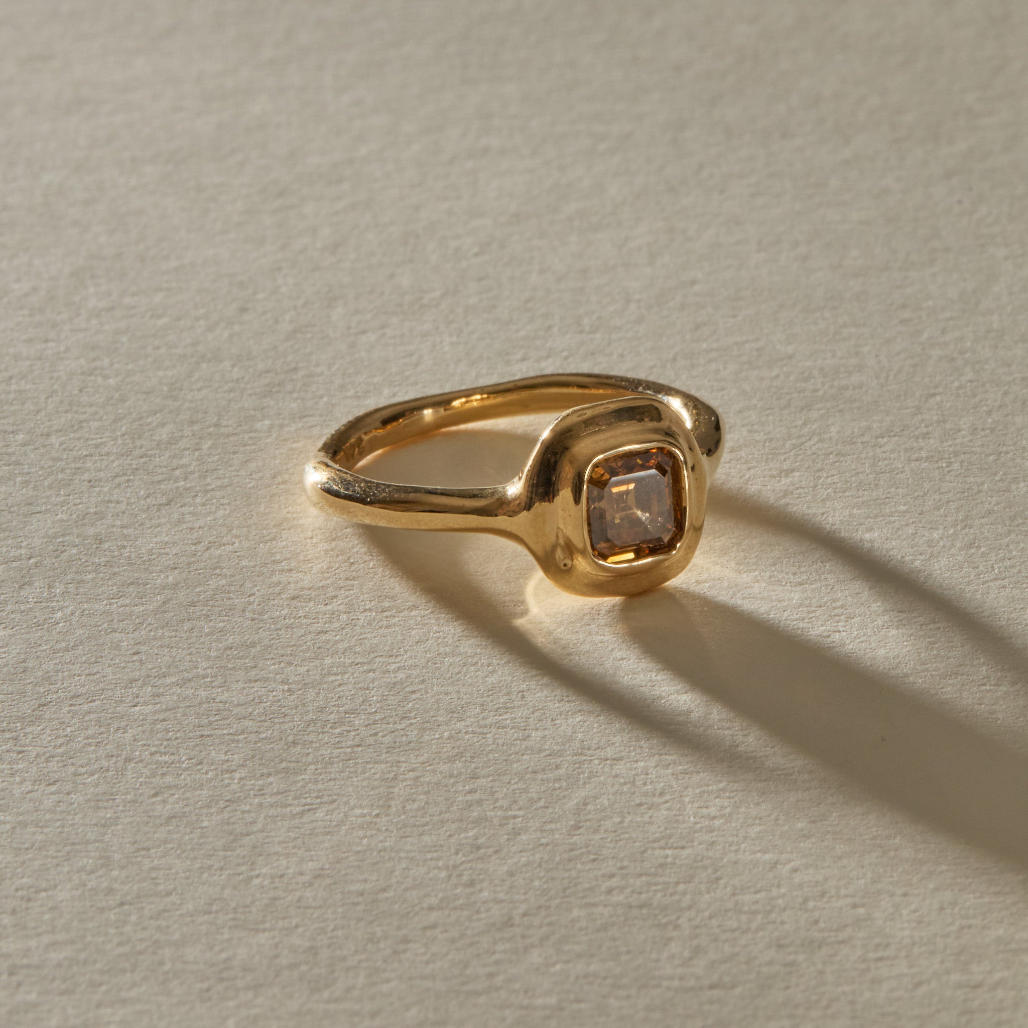 Ambre Ring in 14k recycled gold with a 1.02ct square step cut champagne diamond in a soft bezel, in warm sunlight.
