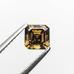 The 1.02ct champagne step cut diamond held in tweezers, showing its golden glow and stepped facets.