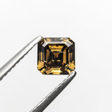 The 1.02ct champagne step cut diamond held in tweezers, showing its golden glow and stepped facets.
