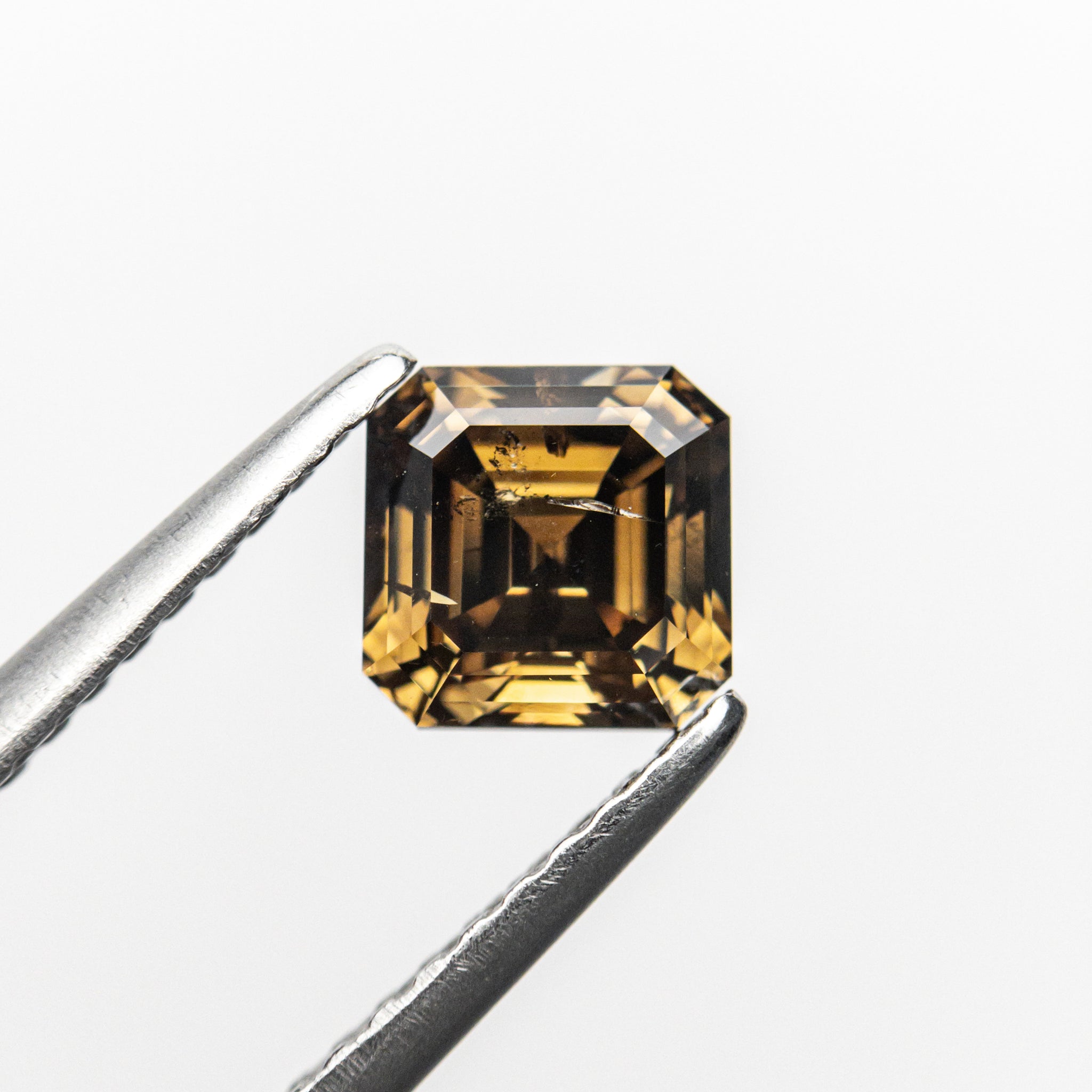 The 1.02ct champagne step cut diamond held in tweezers, showing its golden glow and stepped facets.