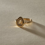 Aurum Pear Diamond Ring from the front, the champagne diamond glowing in warm light.