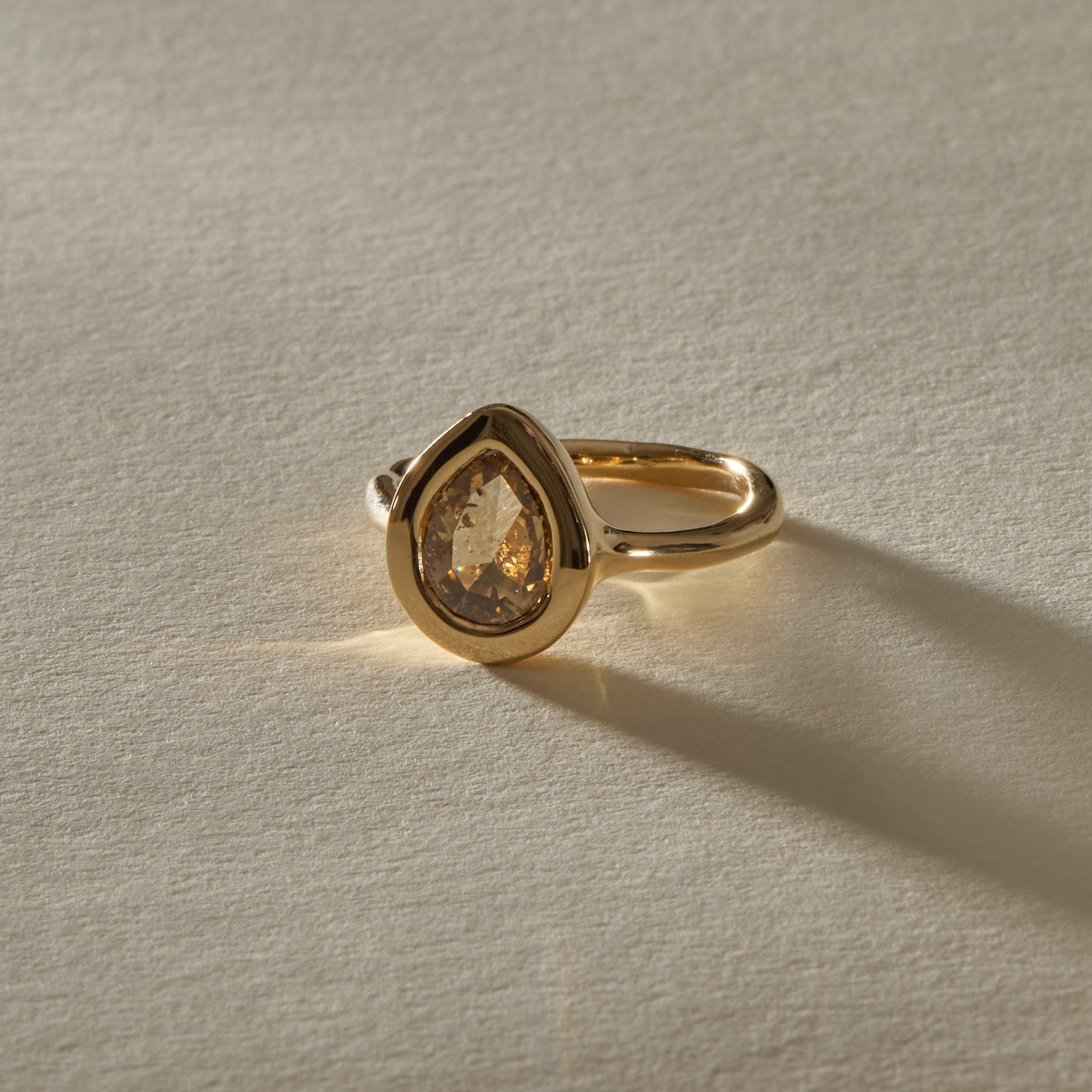 Aurum Pear Diamond Ring from the front, the champagne diamond glowing in warm light.