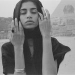 Model with her hands to her face before the pyramids, wearing a Black Tourmaline Amulet Ring and stacked gold rings.