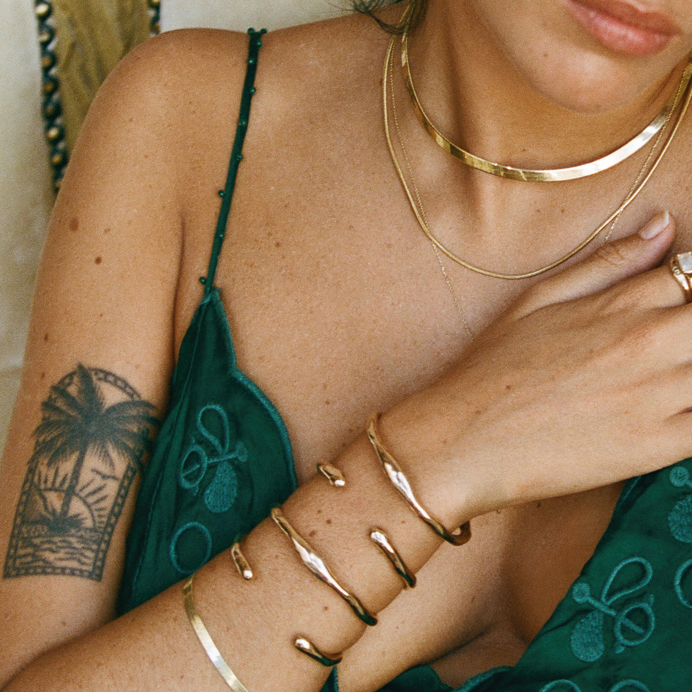Bone Cuff Bracelet stacked with bangles on a model in a green top, layered with gold necklaces.