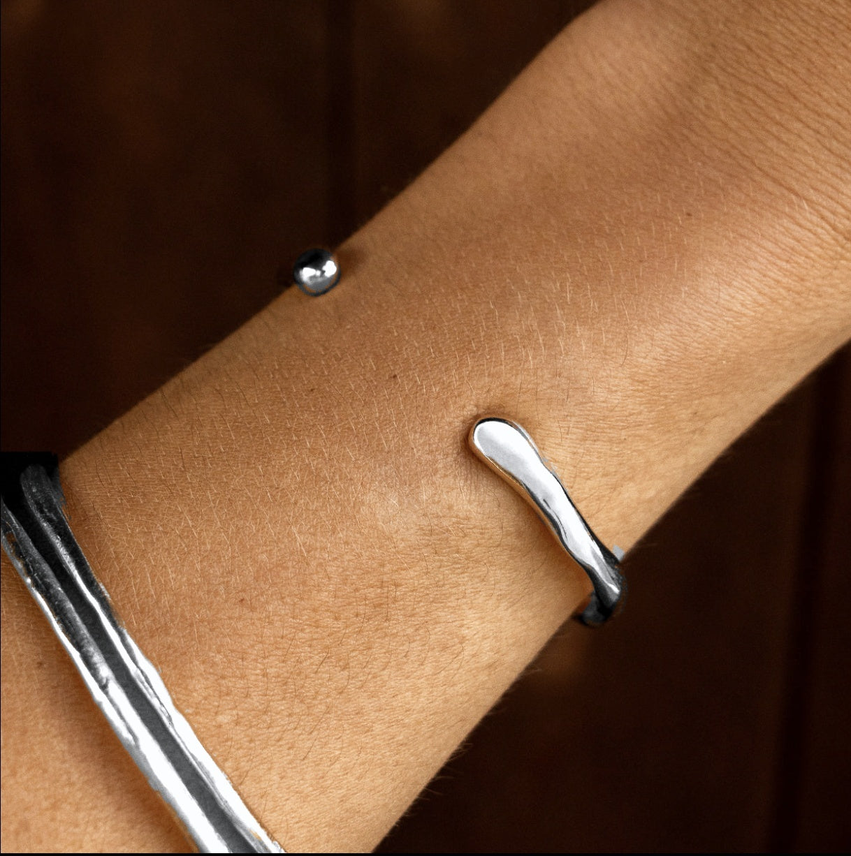 Sterling silver Bone Cuff Bracelet worn on the wrist with silver bangles, against a dark background.