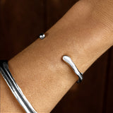 Sterling silver Bone Cuff Bracelet worn on the wrist with silver bangles, against a dark background.