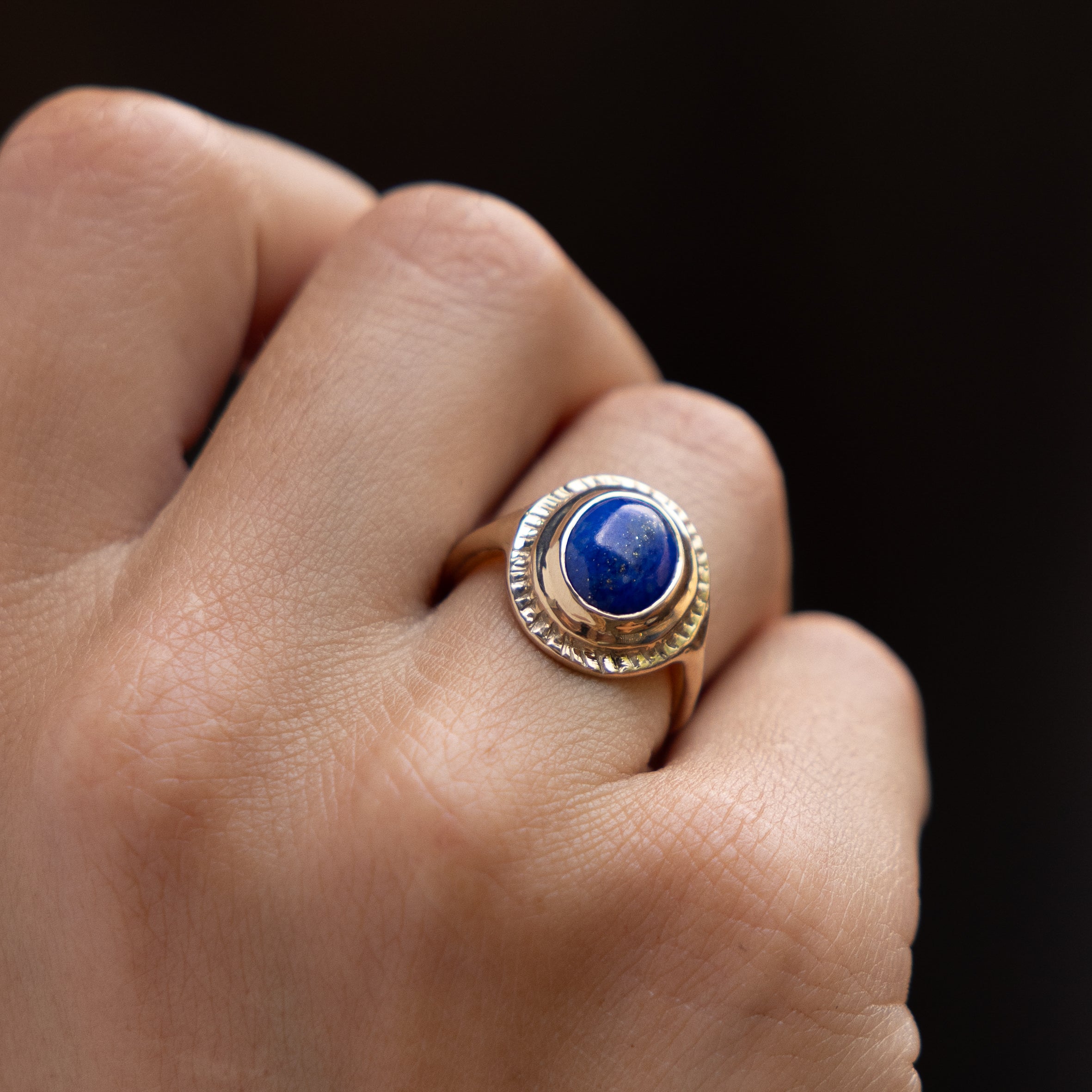 Close up of a hand wearing the Cleo Lapis Lazuli Amulet Ring against a dark background.