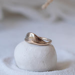 Devotions Wave Ring in recycled bronze resting on a smooth white stone.