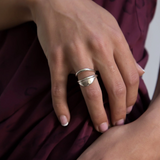 Hand resting on burgundy fabric wearing the Devotions Wave Ring stacked with another ring.