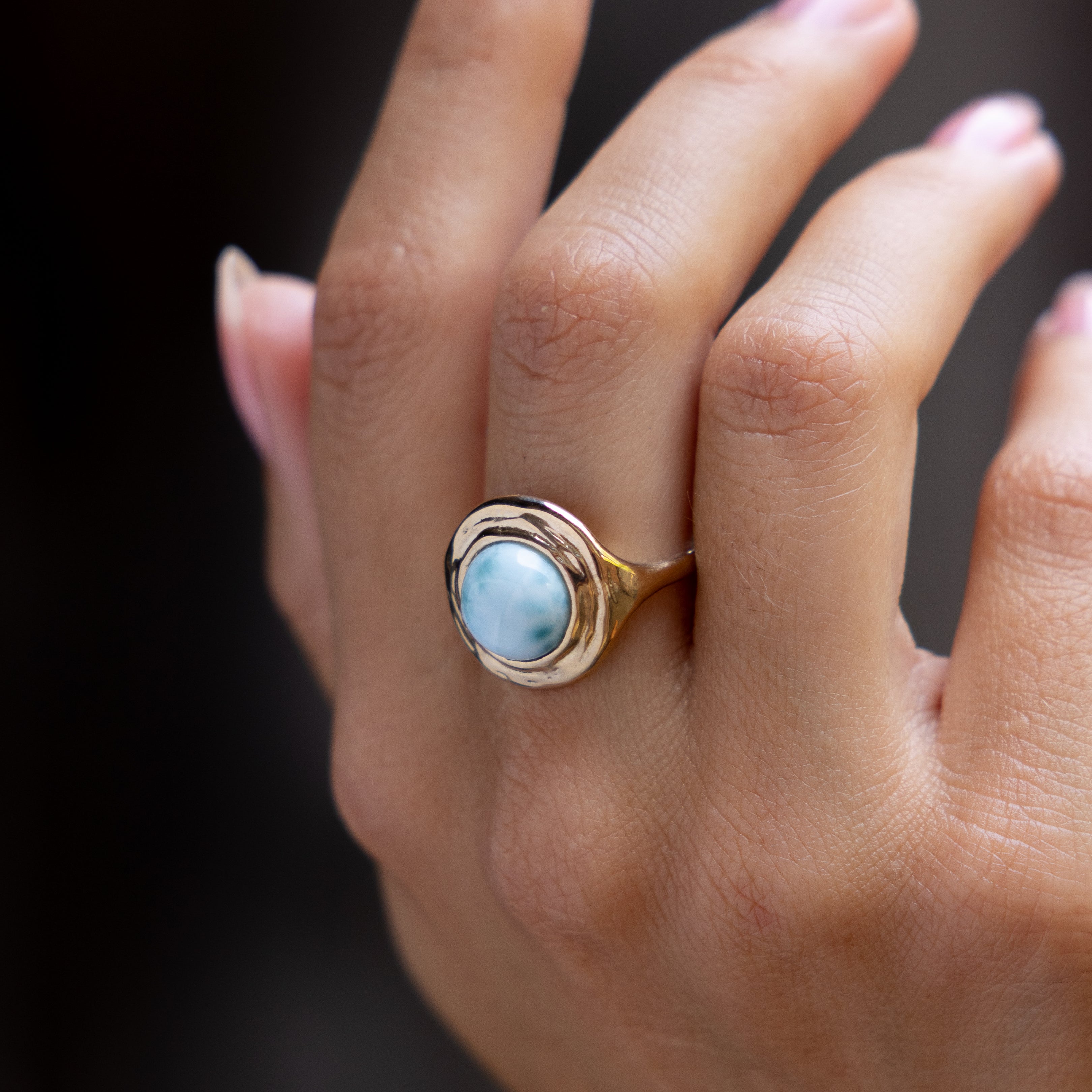 Hand against a dark background wearing the Elysian Larimar Signet Ring.