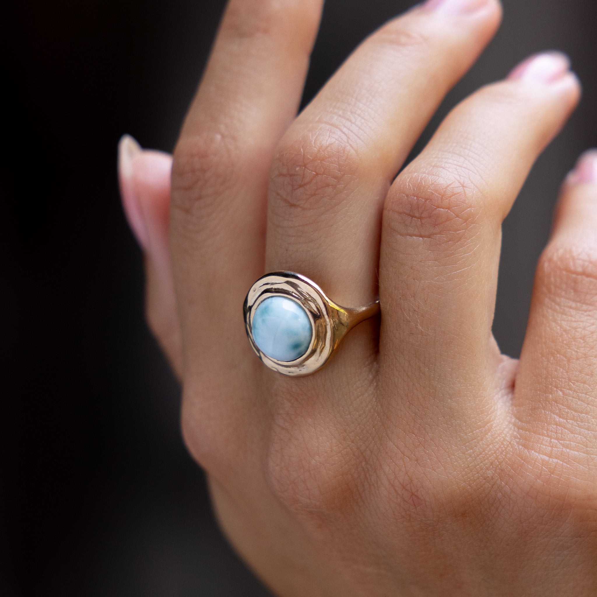 Hand against a dark background wearing the Elysian Larimar Signet Ring.