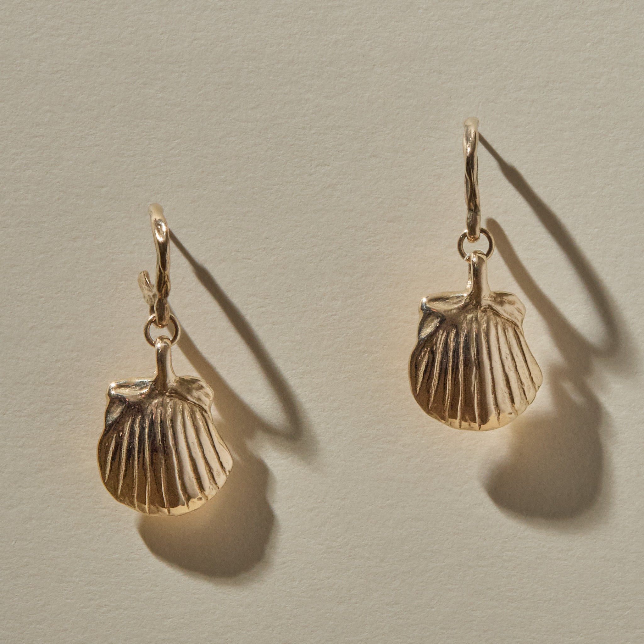 Elysian Shell Hoop Earrings in gold hanging side by side, scallop shells below small hoops.