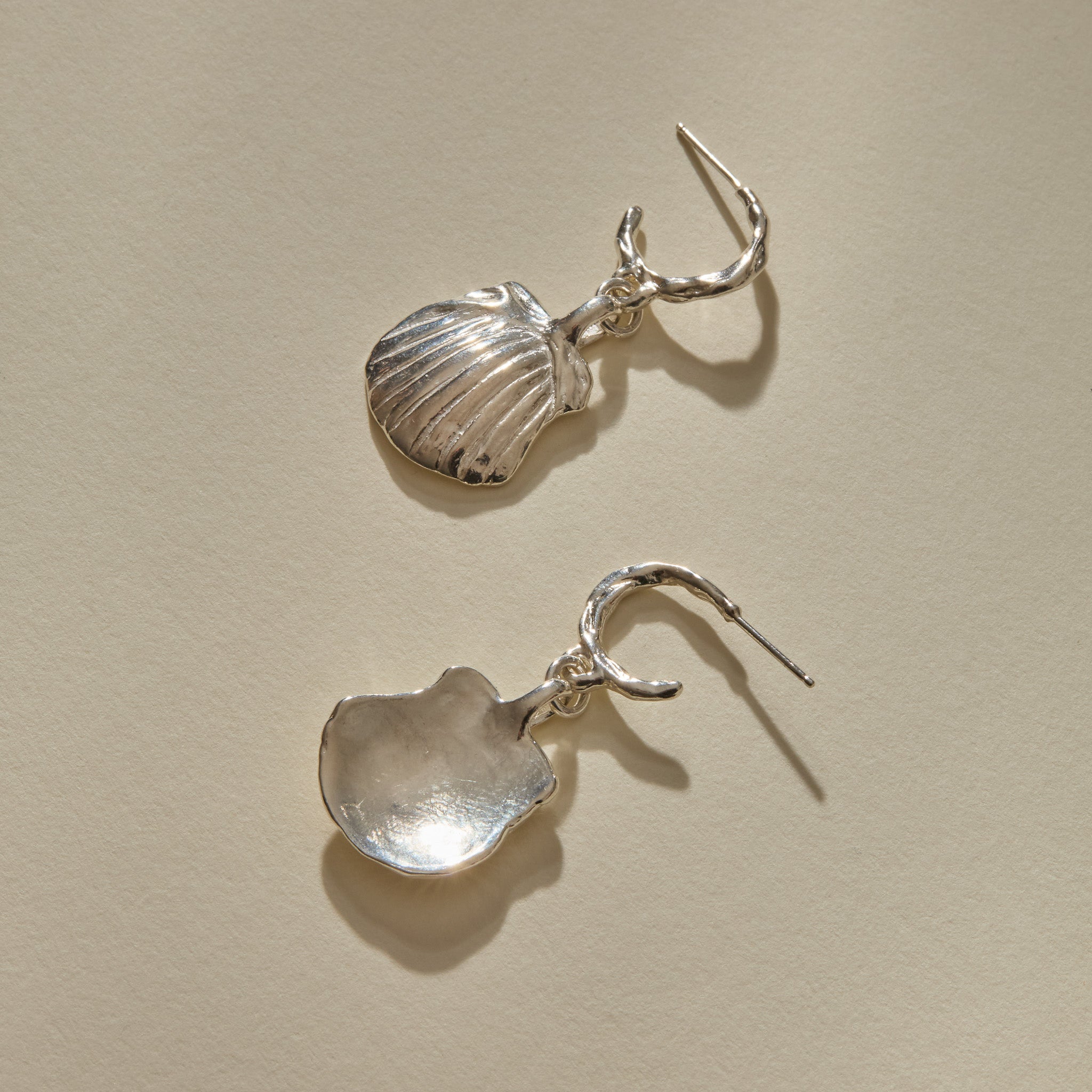 Elysian Shell Hoop Earrings in sterling silver, one shell turned to show its smooth inside.