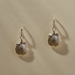 Elysian Shell Hoop Earrings in sterling silver hanging side by side, scallop shells below small hoops.