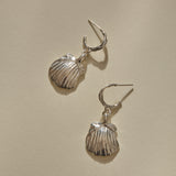 Elysian Shell Hoop Earrings in recycled sterling silver, cast scallop shells on slim hoops, laid flat.