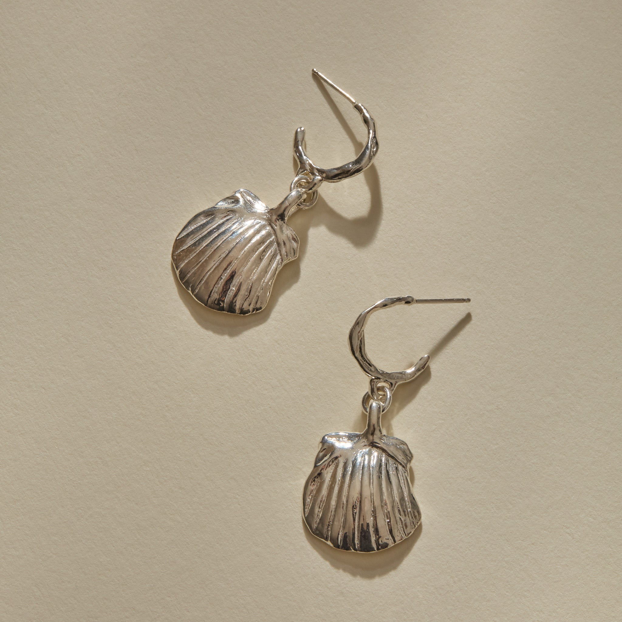 Elysian Shell Hoop Earrings in recycled sterling silver, cast scallop shells on slim hoops, laid flat.
