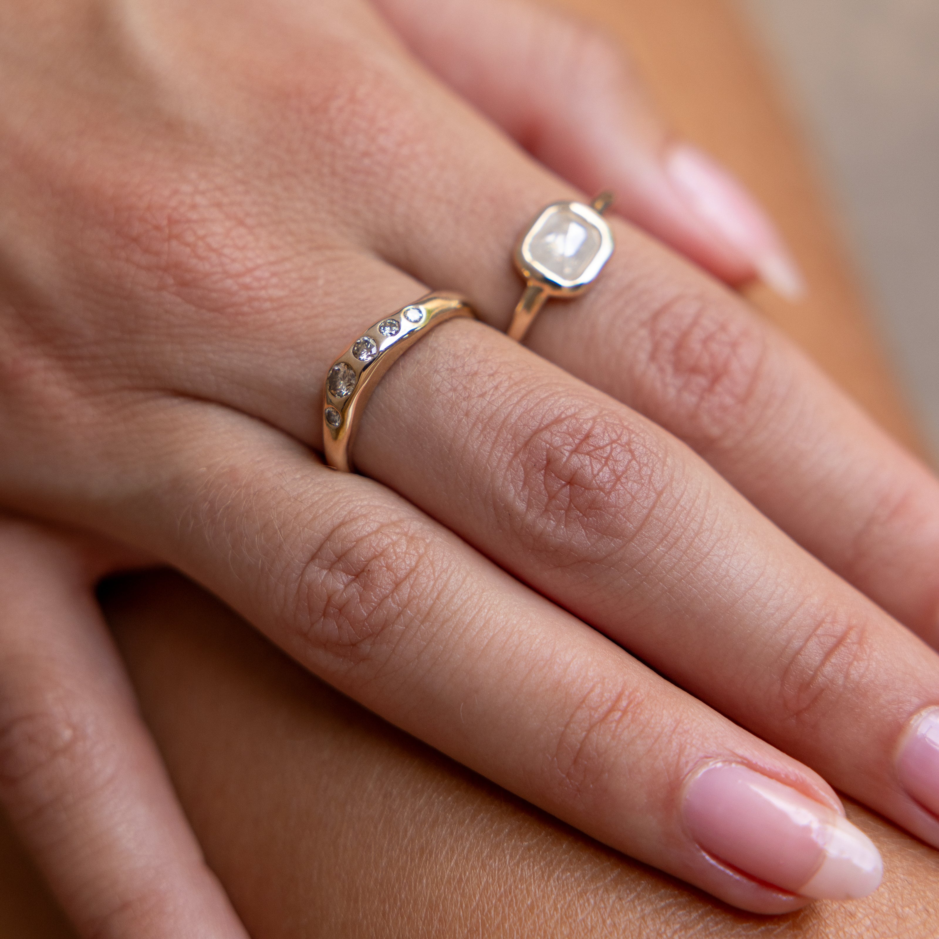 Hands resting on a knee, wearing the Eros Five-Stone Champagne Diamond Band stacked with a pearl ring.