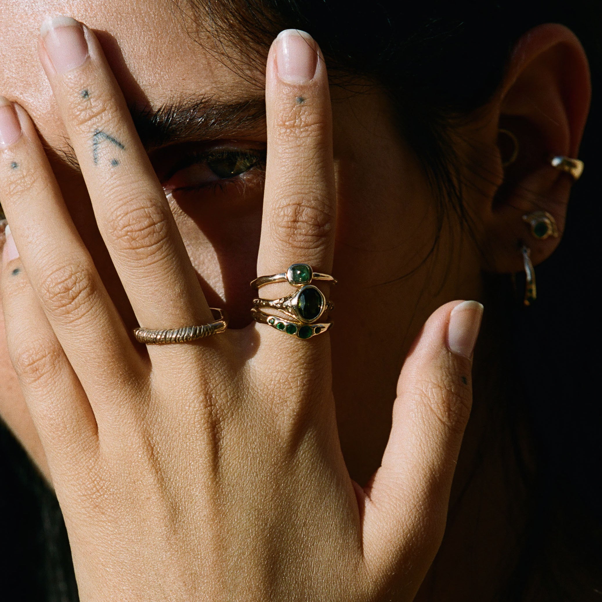 Model with her hand across her face, wearing the Eros Five-Stone Emerald Band stacked with other rings.