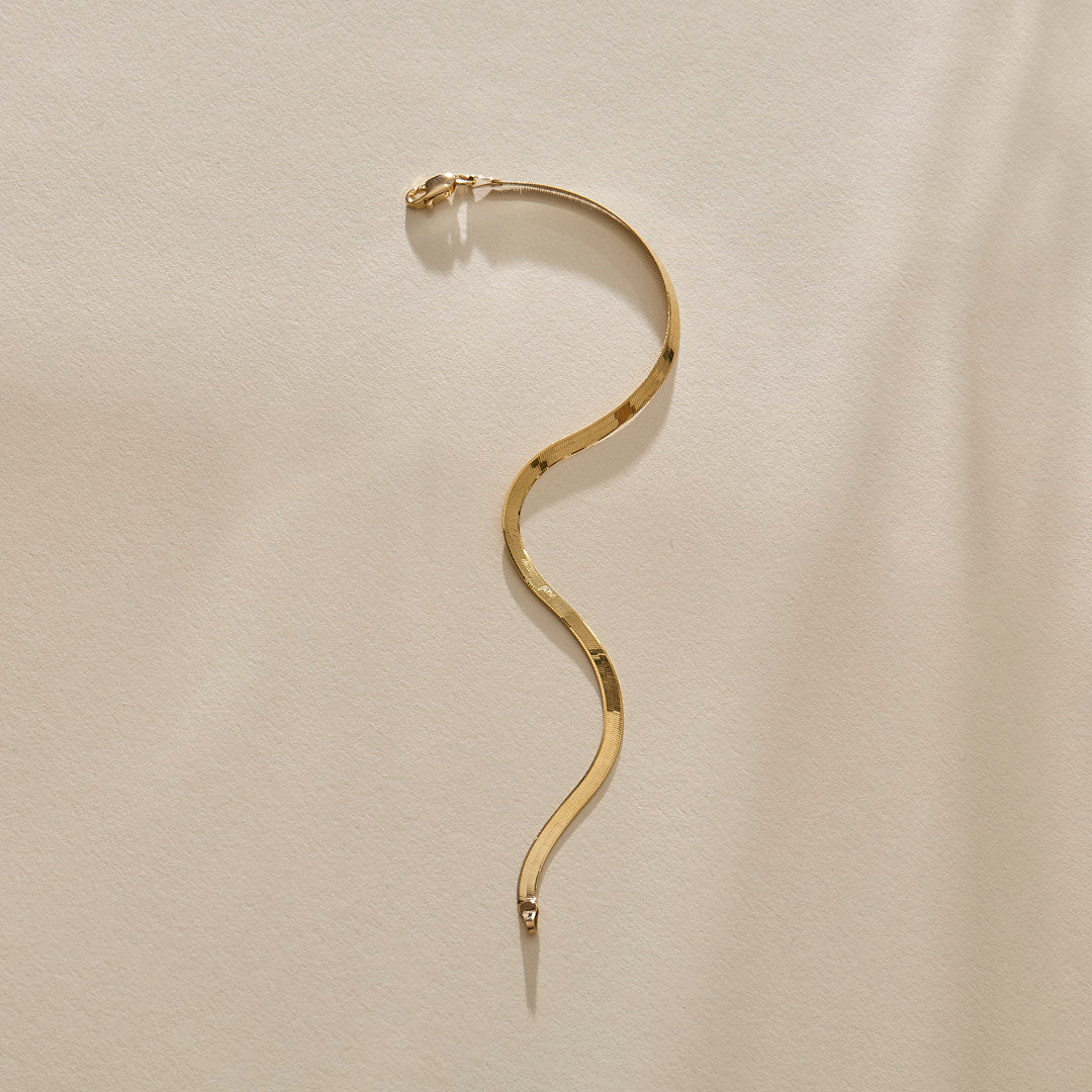 Fehu Herringbone Chain Bracelet in gold laid in an S curve.
