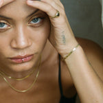 Model with her hand to her head wearing the gold Fehu Herringbone Chain Bracelet and layered gold necklaces.