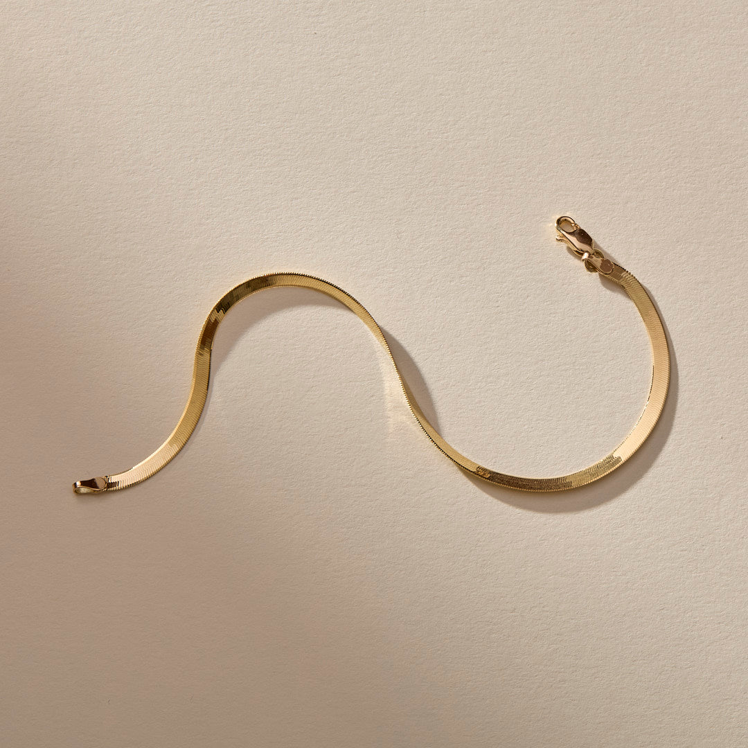Fehu Herringbone Chain Bracelet in gold laid in a wave, showing the flat, shiny herringbone links.