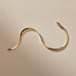 Fehu Herringbone Chain Bracelet in gold laid in a wave, showing the flat, shiny herringbone links.