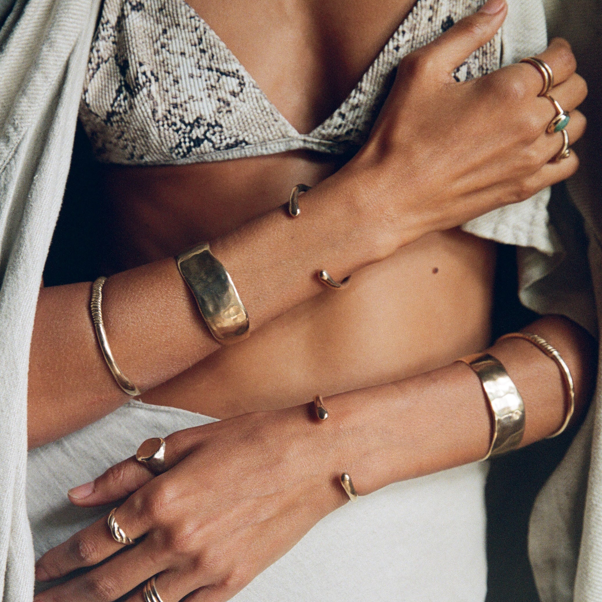 Close up of a model's crossed arms wearing the Guardian Hammered Cuff stacked with bangles and rings.
