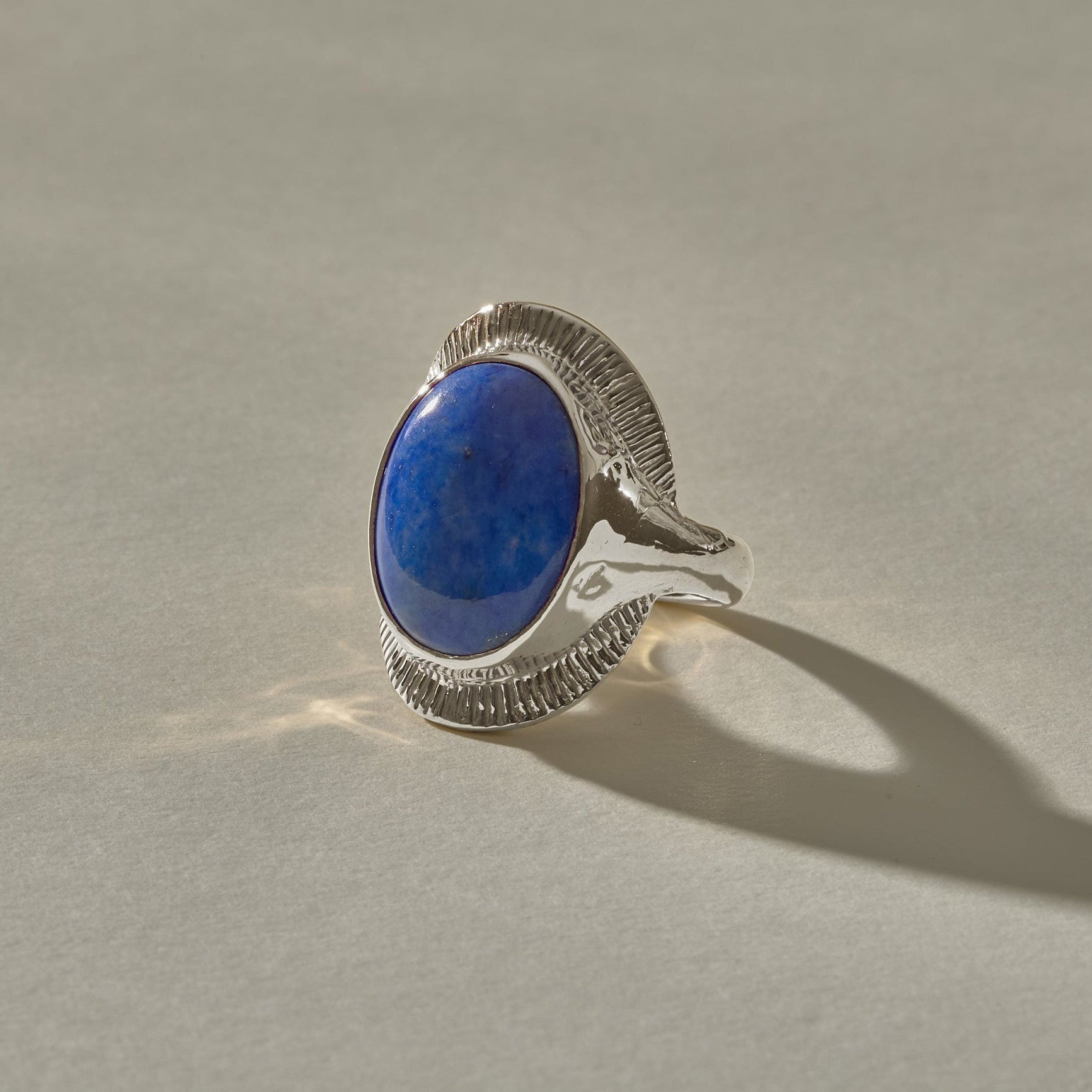 Inanna Lapis Shield Ring in recycled sterling silver, an oval Chilean lapis lazuli cabochon framed by a fine carved sunburst setting.
