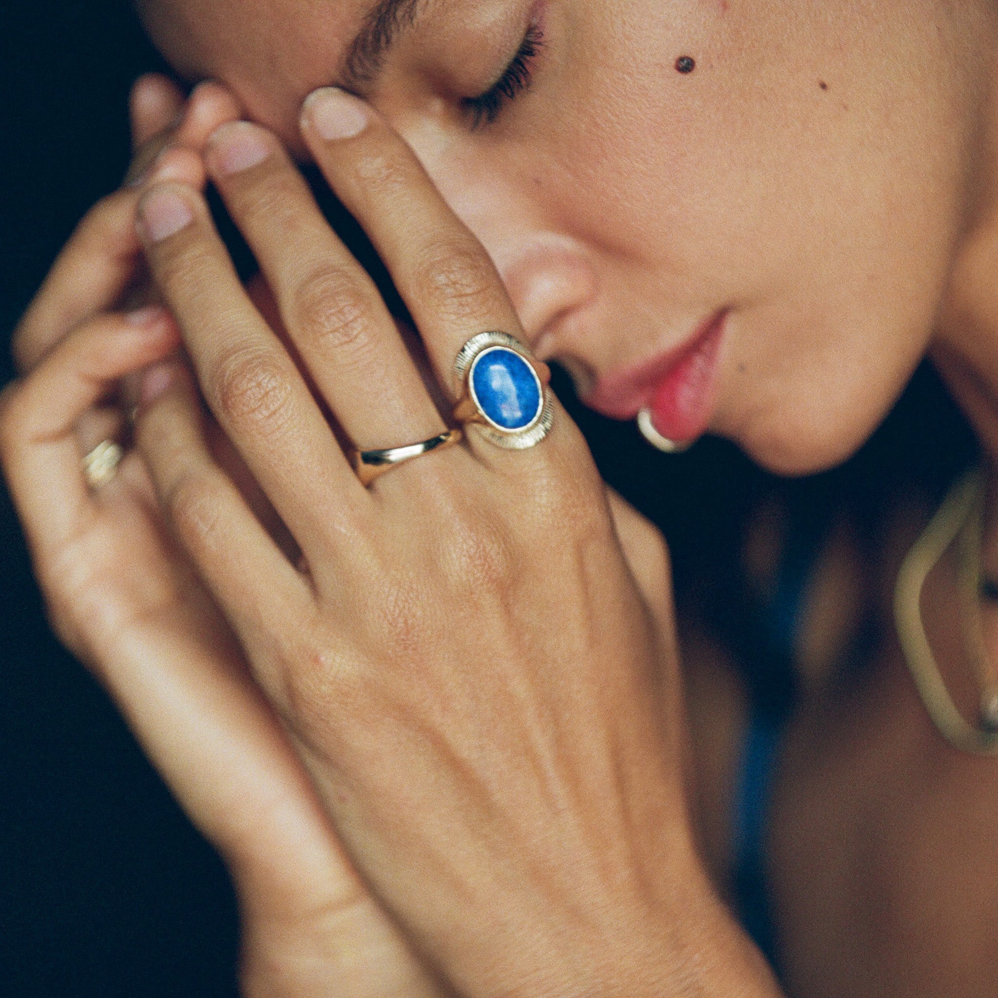 Model with her eyes closed and hands at her face, wearing the gold Inanna Lapis Shield Ring.