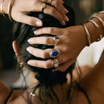 Model with her hands in her hair, wearing the Inanna Lapis Shield Ring stacked with other rings and bangles.