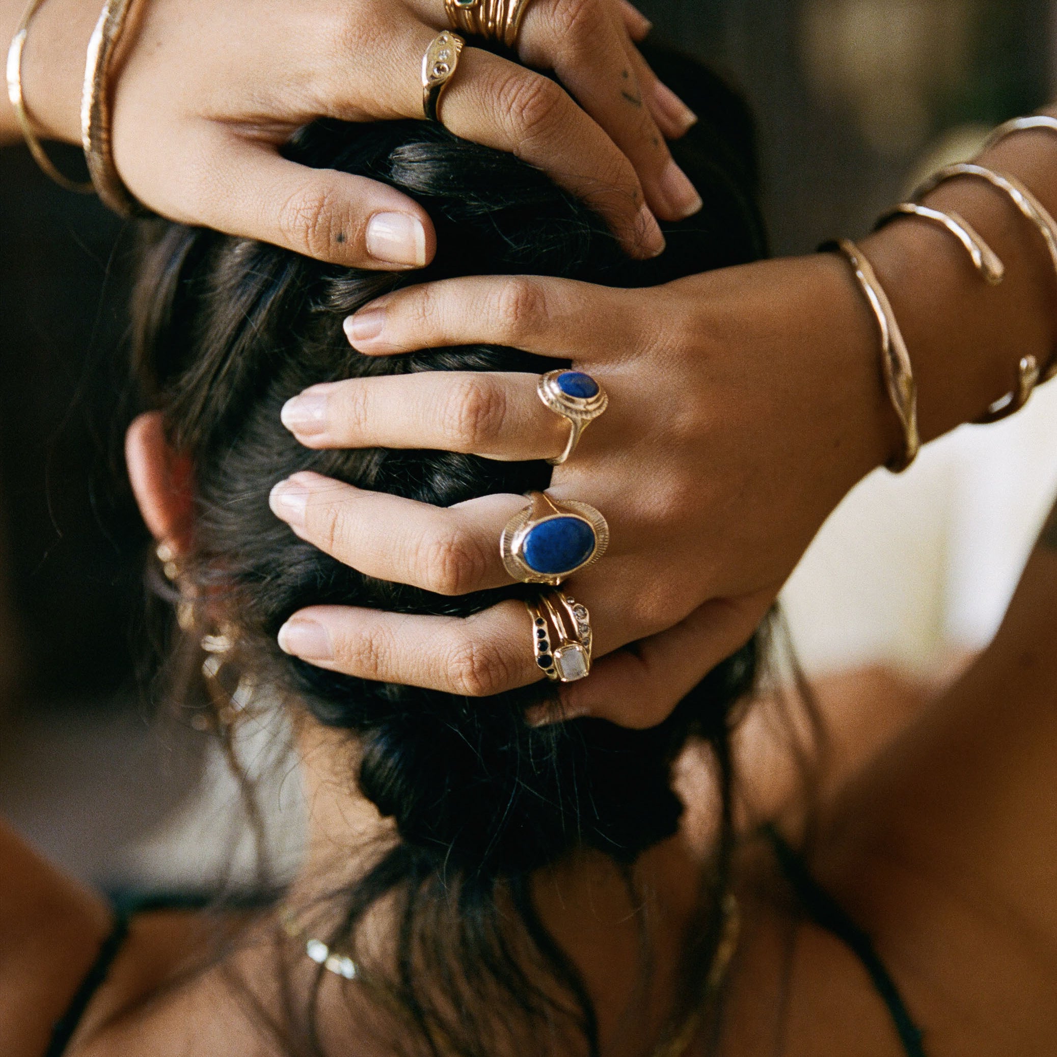 Model with her hands in her hair, wearing the Inanna Lapis Shield Ring stacked with other rings and bangles.