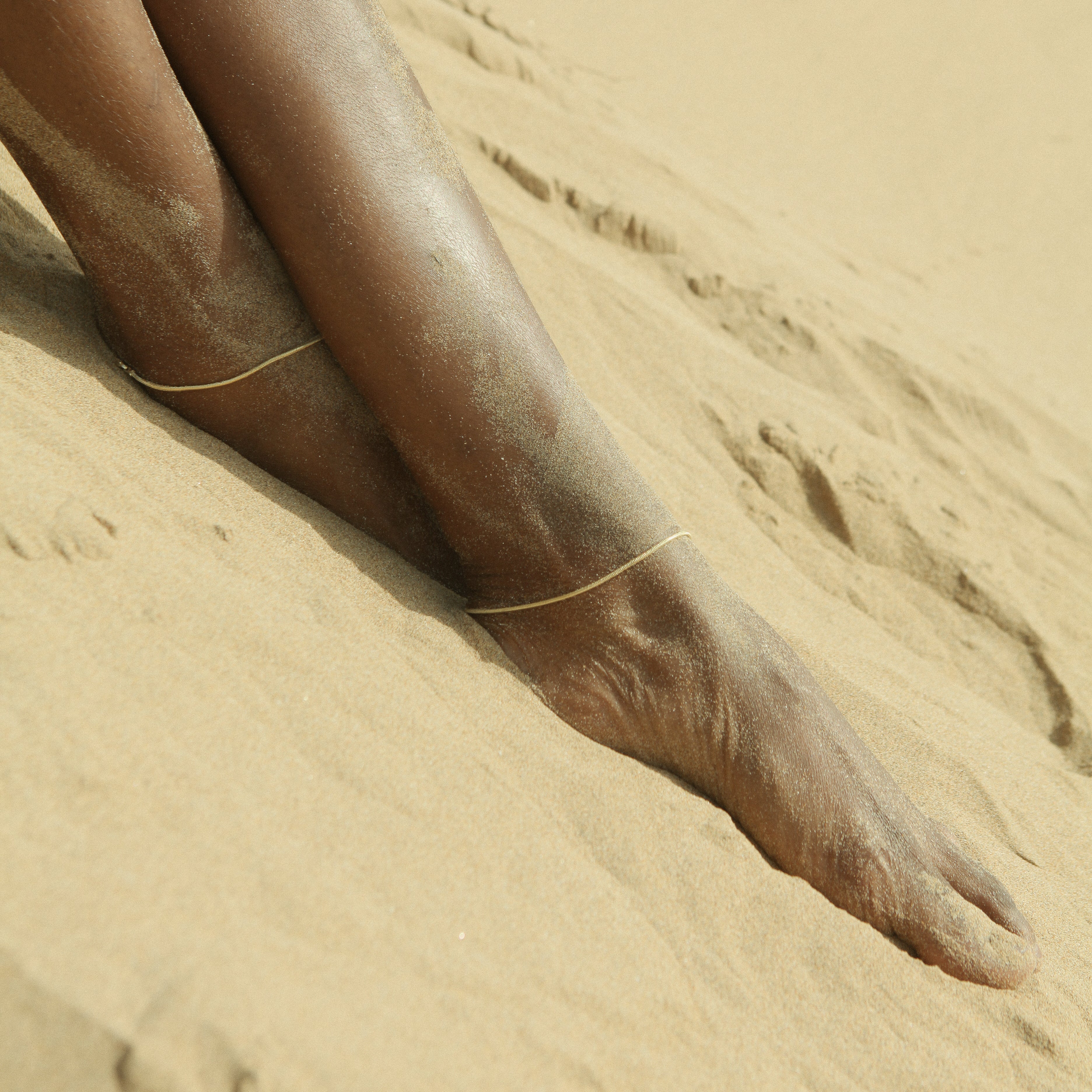 Bare feet in the sand wearing the gold Jera Snake Chain Anklet.