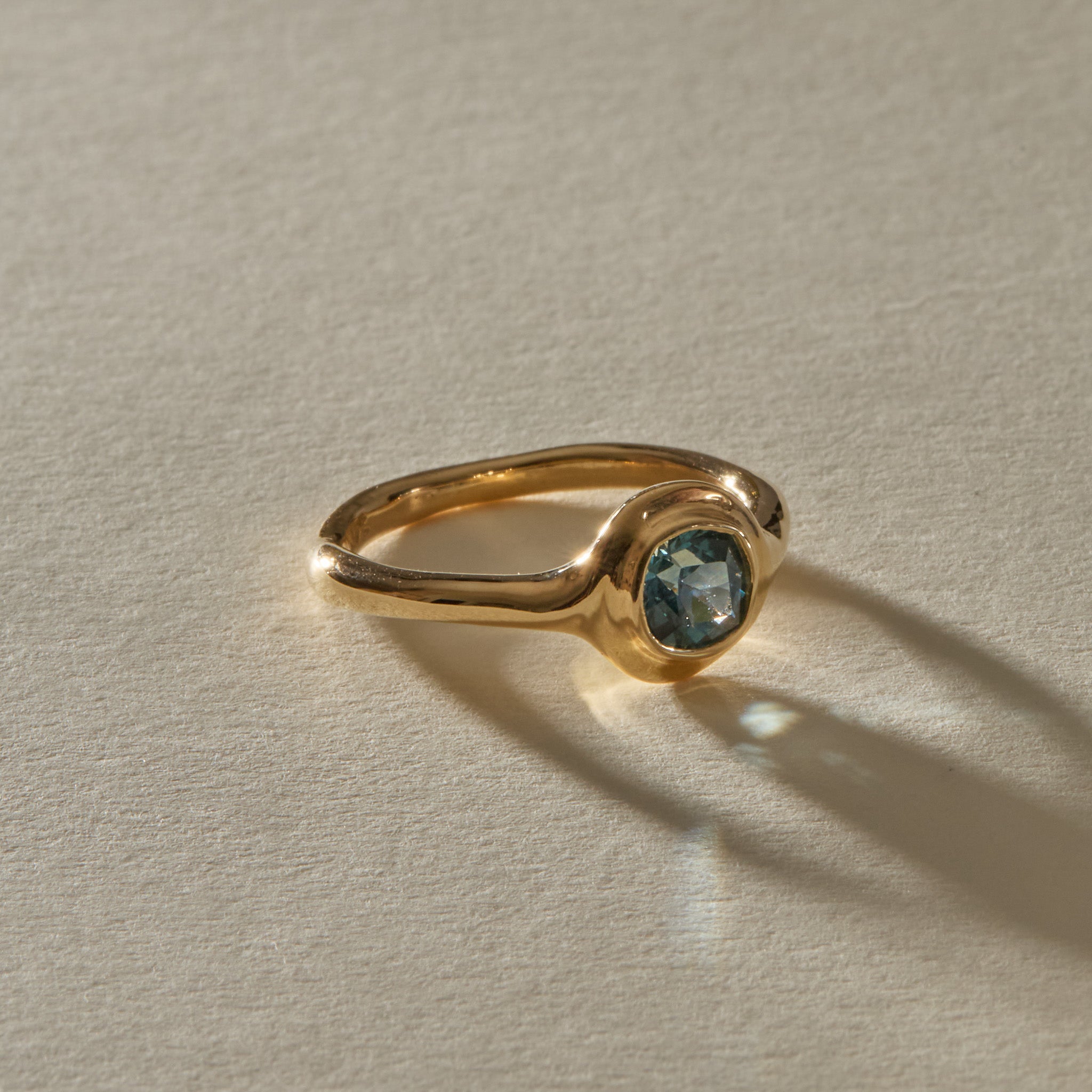 Meridian Ring in 14k recycled gold, a 0.82ct blue-teal cushion cut Montana sapphire in a bold bezel on an organic band, in warm sunlight.
