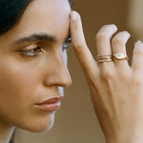 Model with her hand at her brow, wearing thin gold stacking rings with the Orion's Belt diamond ring.