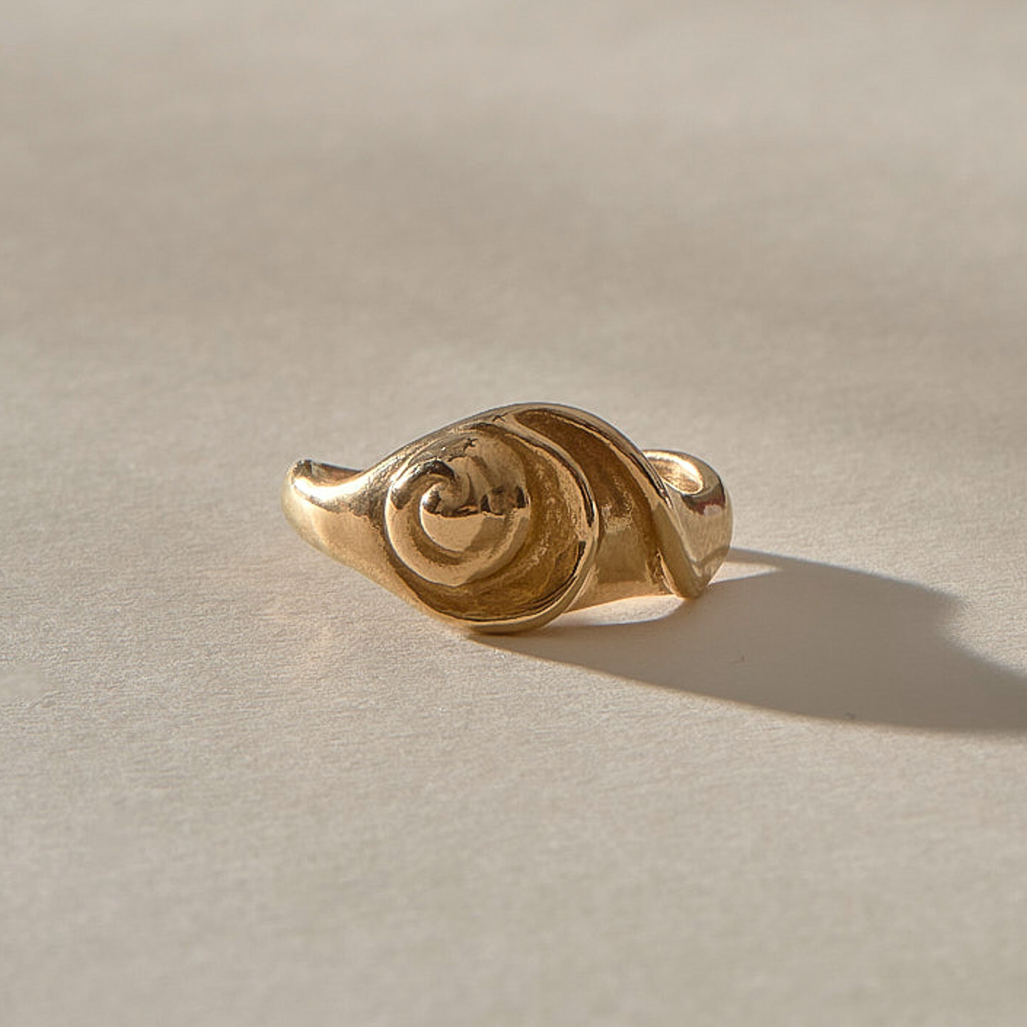 Neptune Spiral Shell Ring in solid recycled gold from a low angle, the spiral shell rising from a wavy organic band.