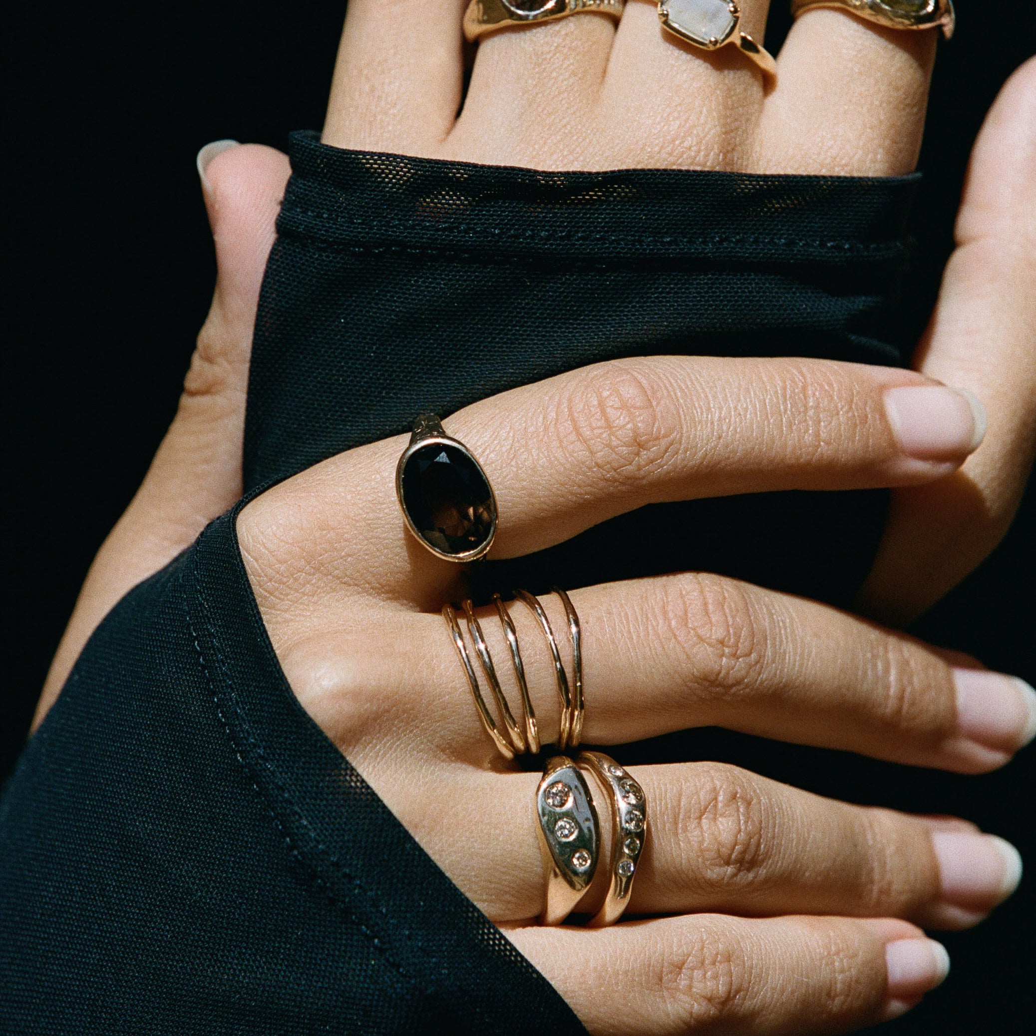 Model's hands against black fabric, wearing Nova stacking rings layered with other Catori Life rings.