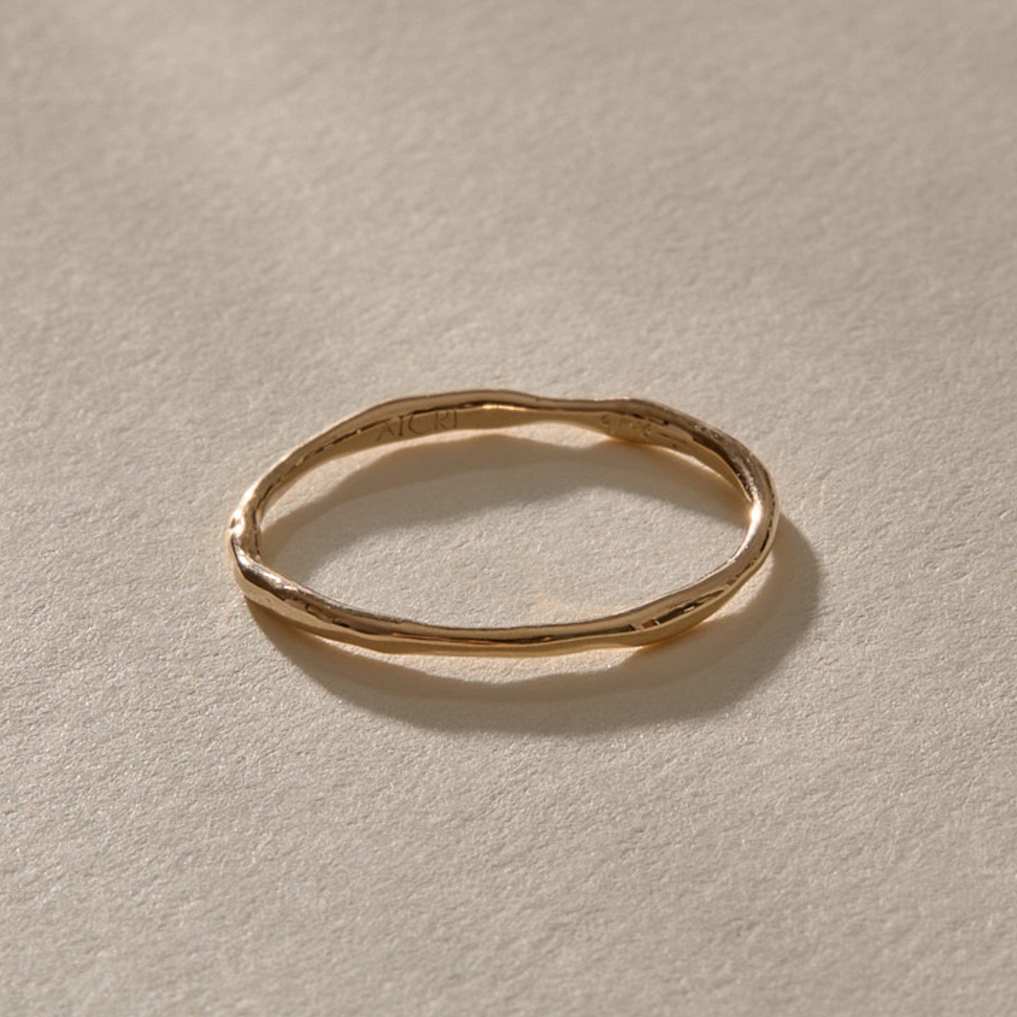 A single Nova stacking ring in solid gold, a delicate 1 to 1.5mm band with a gently uneven shape.