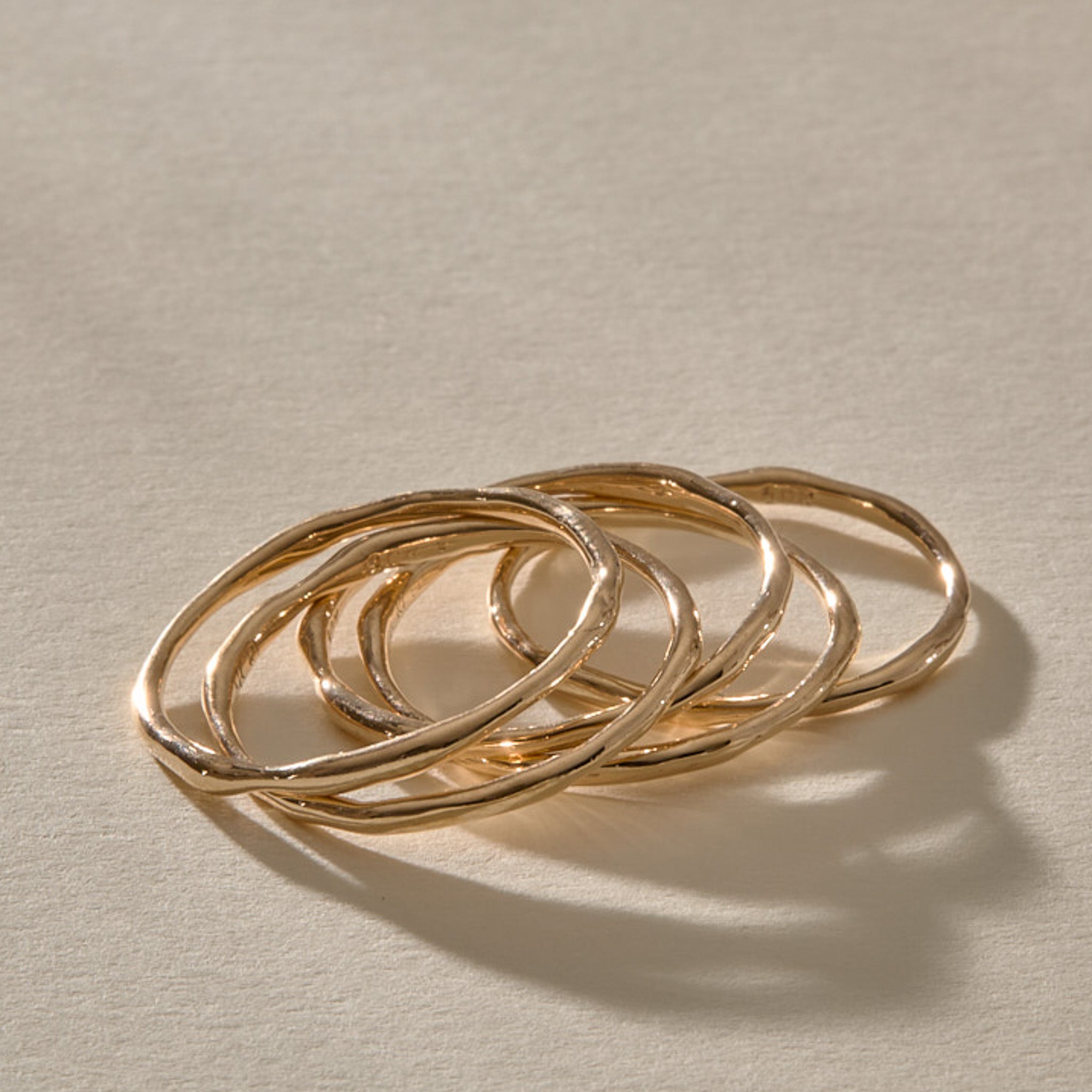 Nova gold stacking rings at an angle, five slim bands layered loosely together.