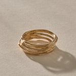 Nova Stacking Rings, a set of five thin, softly imperfect bands in solid recycled gold, stacked together in warm sunlight.