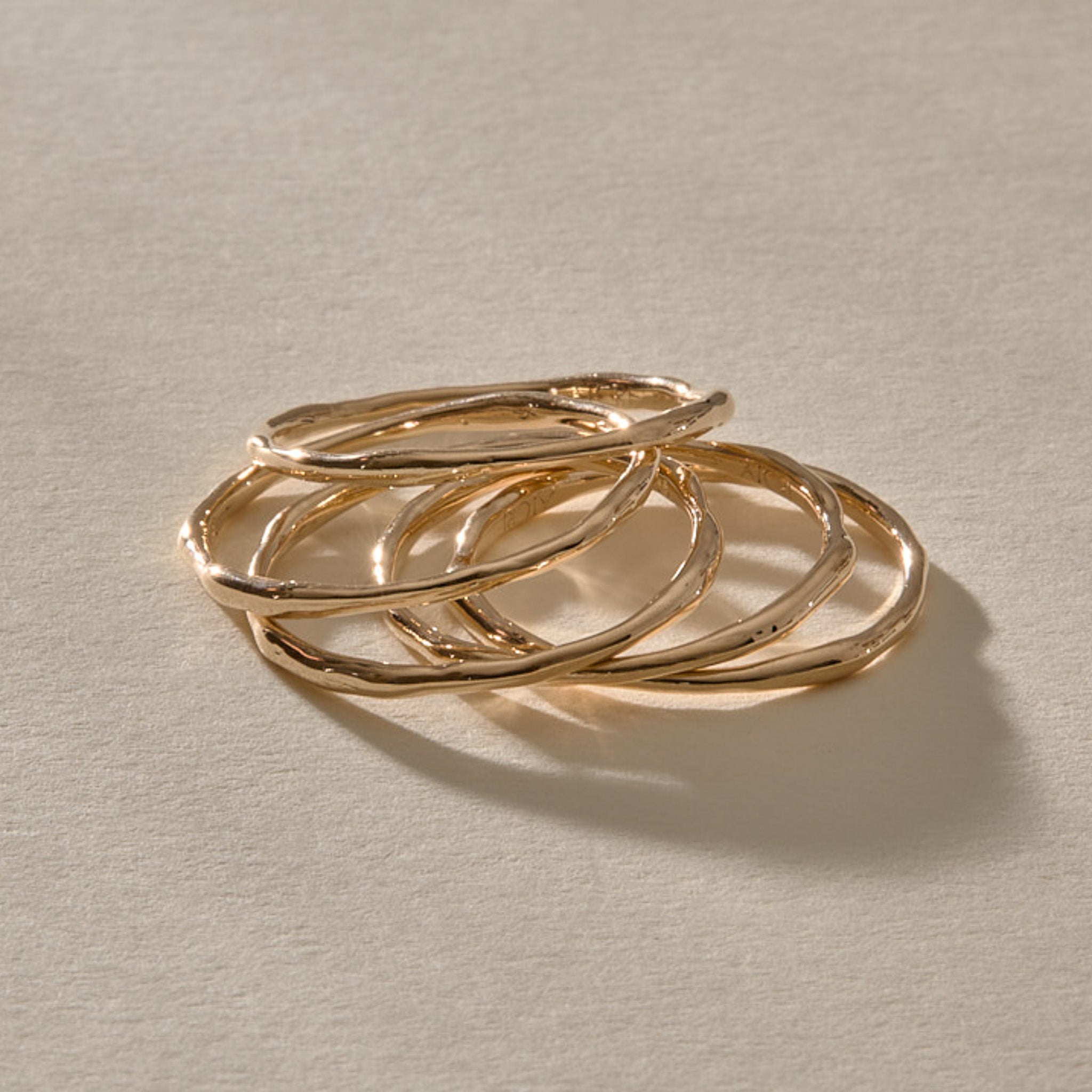 Five Nova gold stacking rings resting together, showing their organic, hand-formed shapes.