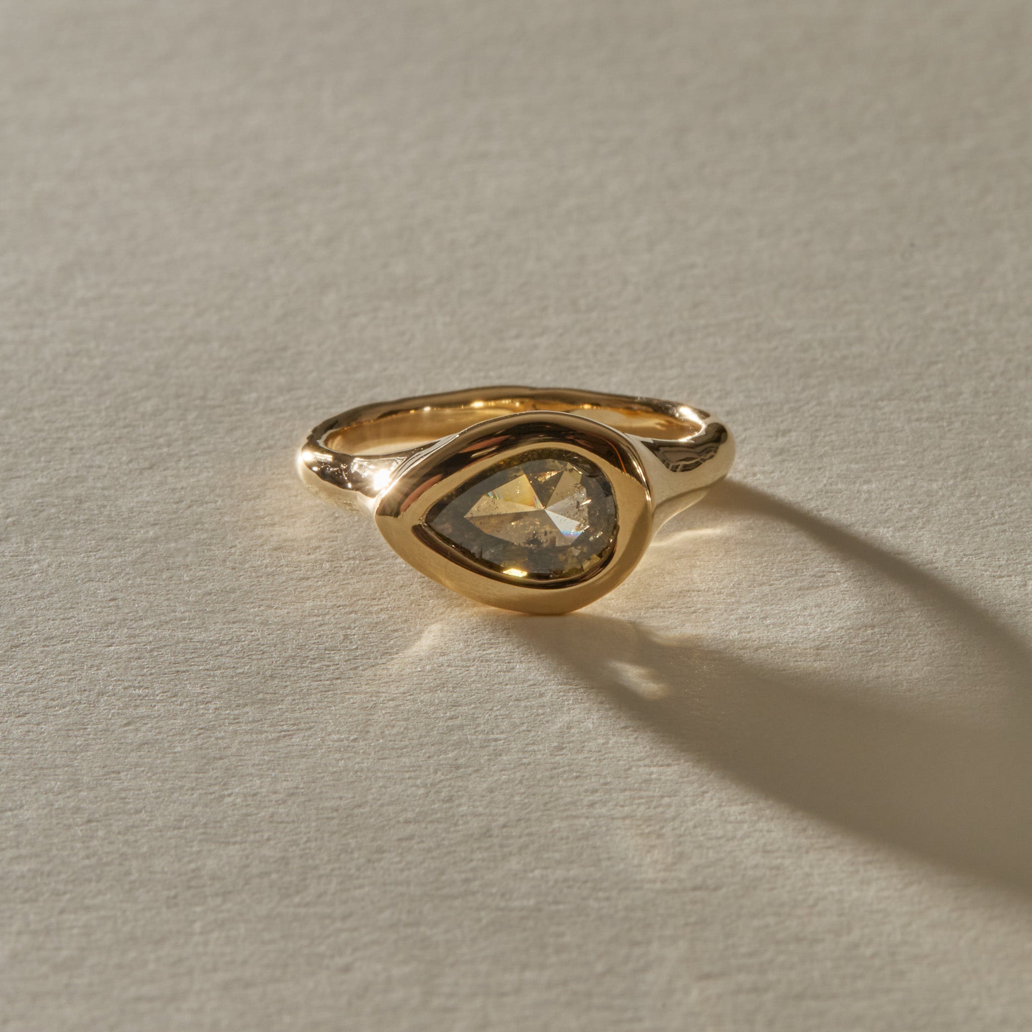 Oriente Ring in 14k recycled gold, a pear shaped rose cut champagne salt and pepper diamond set east to west in a bold bezel, in warm sunlight.