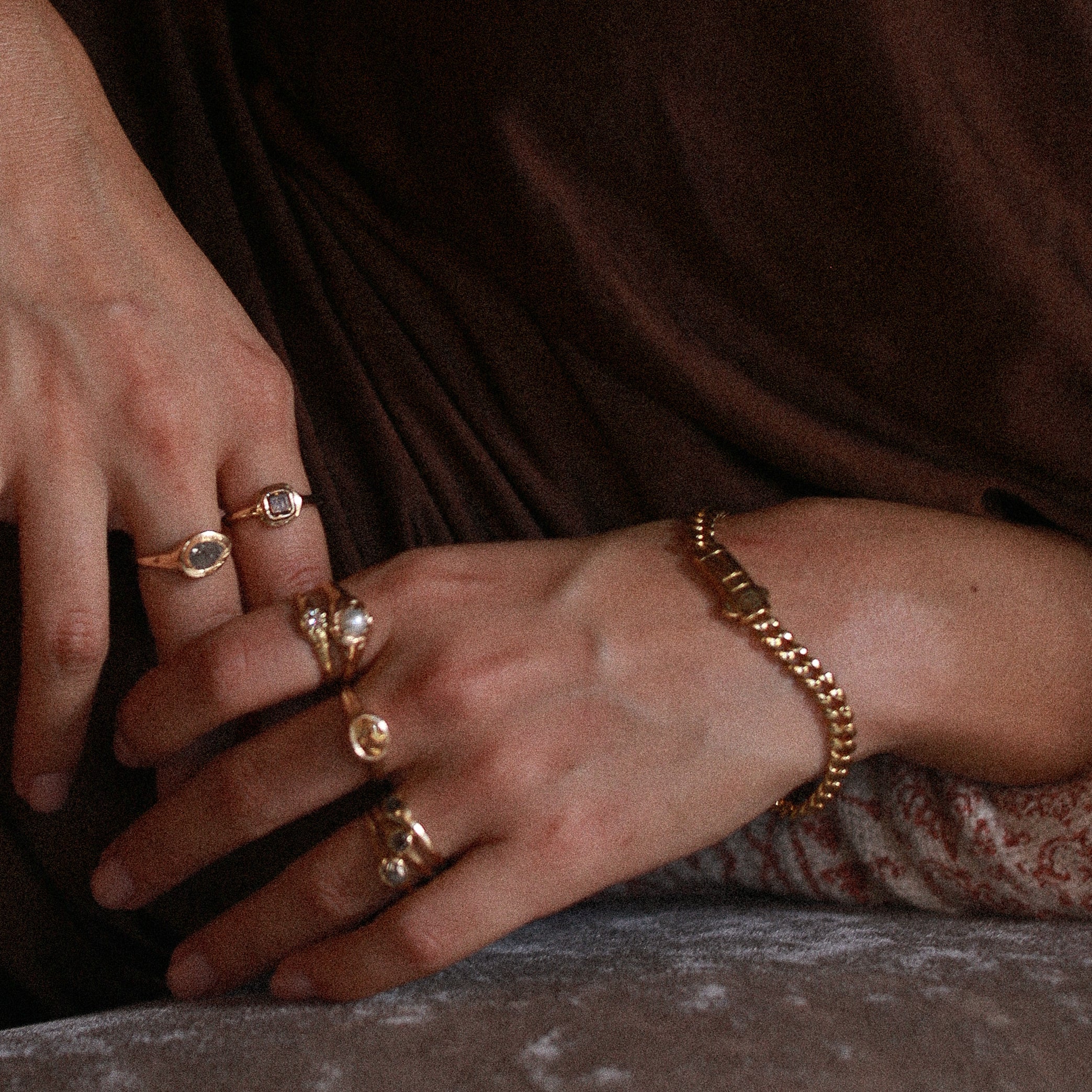 Oro Sagrado Cuban Link Bracelet in 14k gold worn on the wrist, hands resting on velvet with gold rings.
