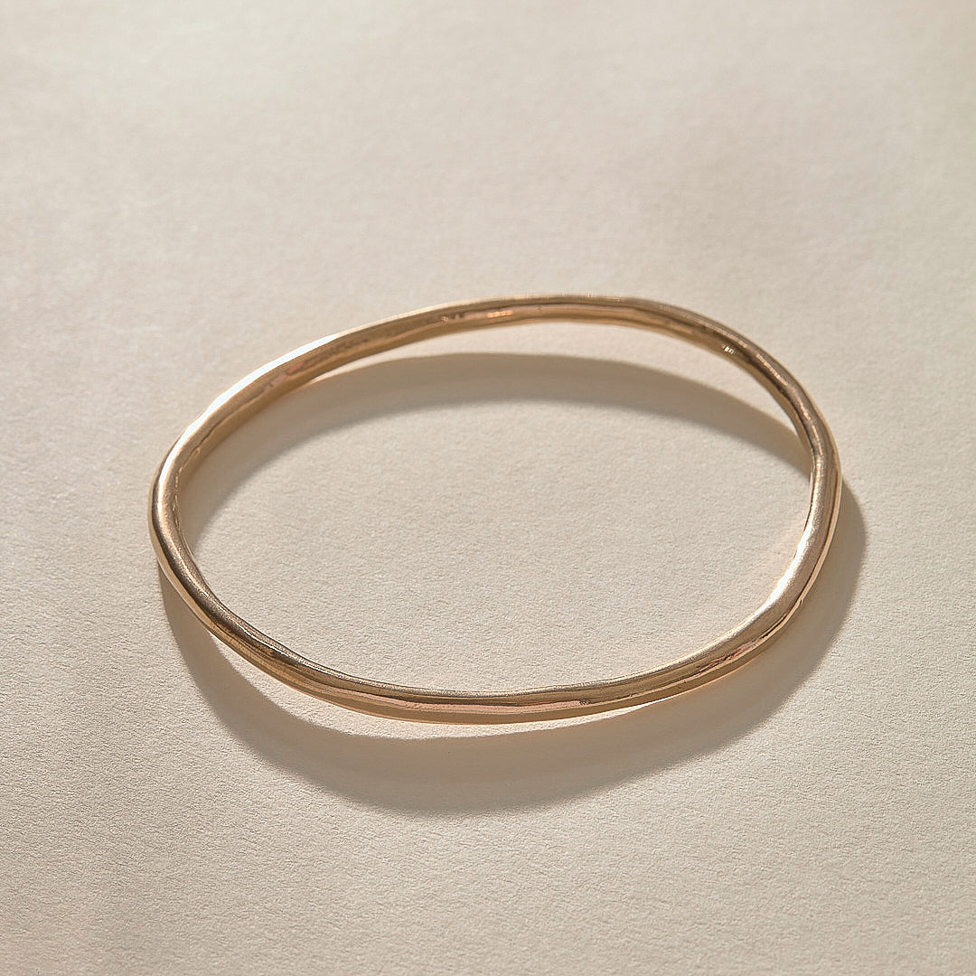 Single Rustic Bangle in bronze at an angle, catching the light on its hand-polished surface.