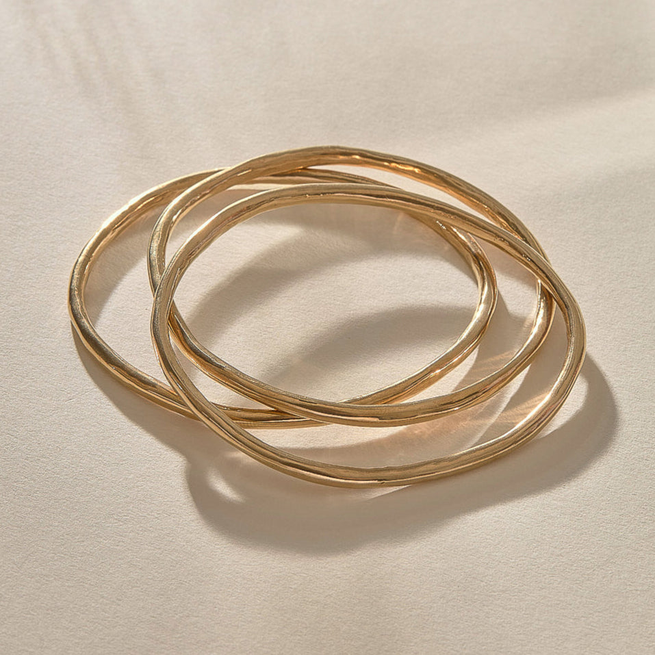 Set of 3 Rustic Bangles in gold at an angle, showing their weight and organic shape.