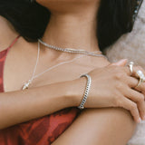 Sagrado Cuban Link Bracelet in sterling silver worn on the wrist, layered with silver necklaces and rings.